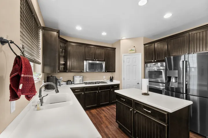 Kitchen featuring dark wood-finish cabinetry, stainless steel appliances, a center island with countertop, recessed lighting, and wood-finish flooring