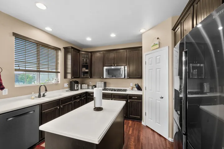 Kitchen featuring dark wood-finish cabinetry, white solid surface countertops, a center island, recessed lighting, and wood-finish flooring