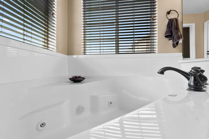 Built-in jetted tub featuring a matte black faucet and dual windows with horizontal blinds