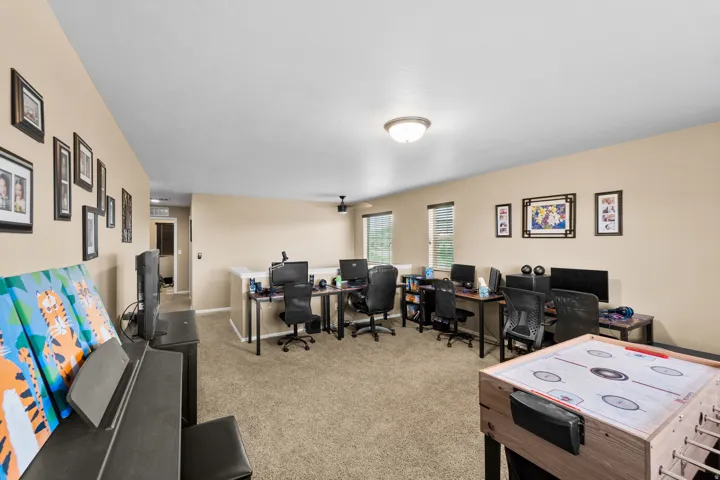 Spacious carpeted room featuring multiple windows with horizontal blinds, a ceiling-mounted light fixture, and a partial low wall