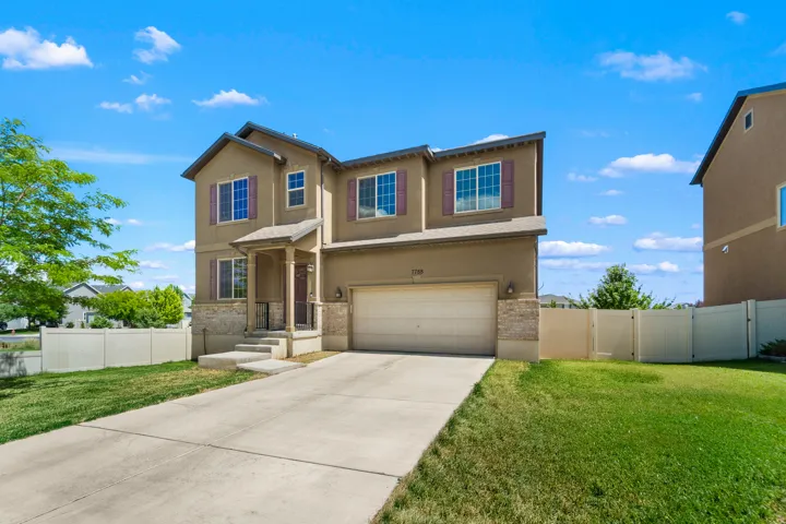 Two-story stucco exterior featuring stone accents, a covered front porch, and a two-car garage