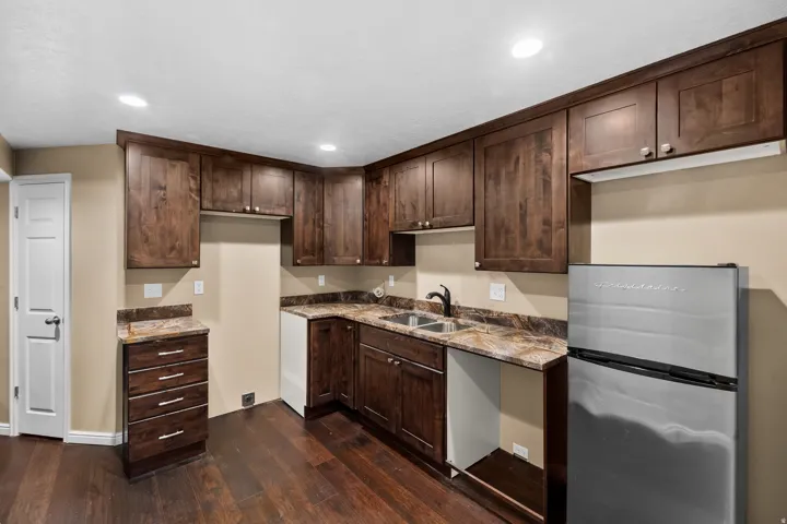 Kitchenette featuring dark wood-finish cabinetry, granite-patterned countertops, a double basin sink with a black faucet, and wood-finish flooring