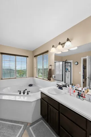 Soaking tub with dual windows, complemented by a vanity with a single basin sink and dark wood-finish cabinetry