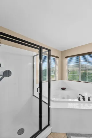 Corner soaking tub with dark bronze fixtures and two windows with blinds