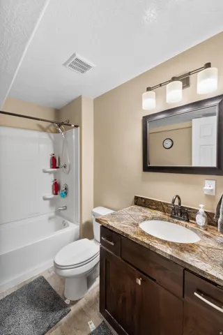 Bathroom featuring a dark wood-finish vanity with a stone countertop, an undermount sink, and a black-framed mirror