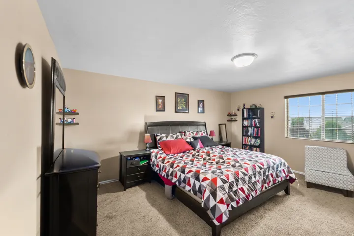 Carpeted bedroom featuring a large window with blinds, a ceiling-mounted light fixture, and neutral-toned walls