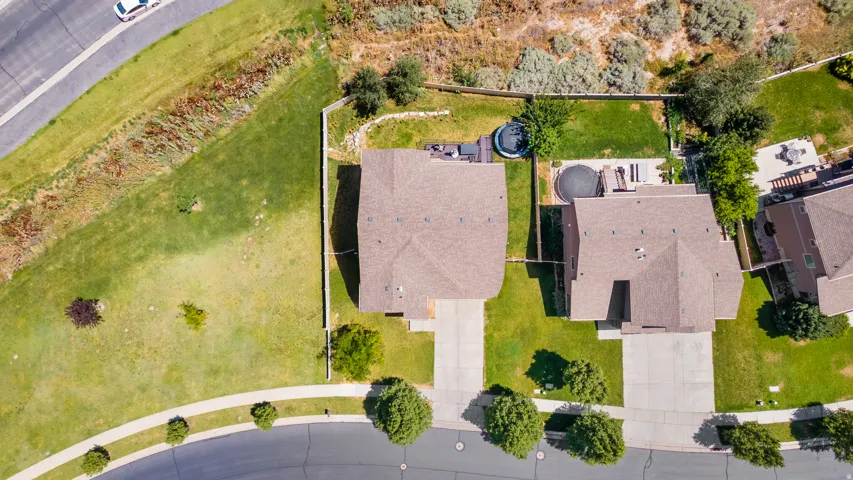Aerial view showcasing two residential properties with brown shingle roofs, concrete driveways, and manicured green lawns