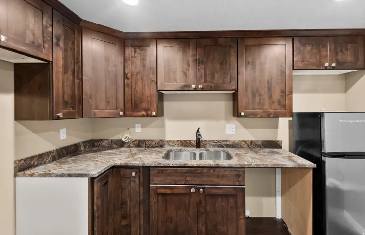 Compact kitchen featuring dark wood cabinetry, a double basin stainless steel sink with a matte black faucet, and patterned countertops with a complementary backsplash