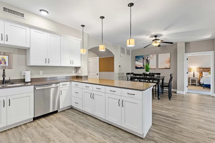 Open-concept kitchen and dining area featuring white shaker-style cabinetry, stainless steel appliances, wood-finish flooring, and a central kitchen island with pendant lighting