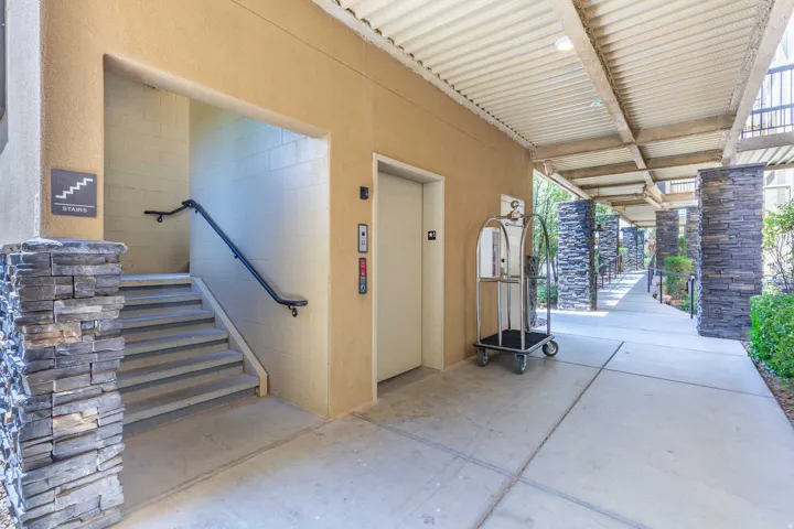 Exterior walkway featuring a covered overhead, elevator access, and a stone veneer column