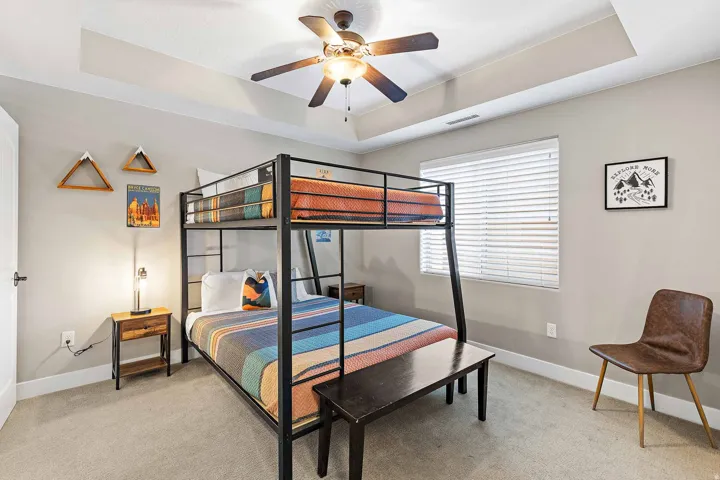 Carpeted bedroom featuring a tray ceiling with a ceiling fan, white window blinds, and a built-in metal bunk bed frame