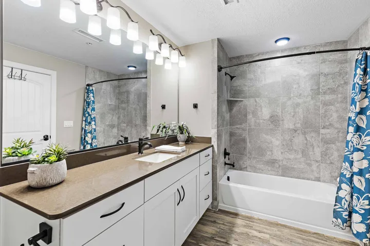Bathroom featuring a white vanity with brown countertop, a large wall-mounted mirror, modern light fixture, and a tiled shower-tub combination with built-in shelf