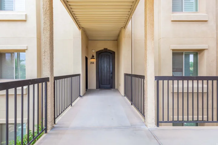 Exterior hallway featuring a dark wood arched entry door with a decorative sconce