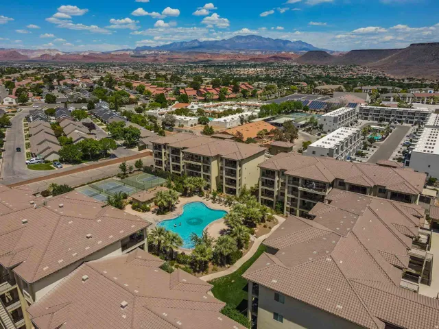 Expansive multi-story complex with a curvilinear swimming pool, surrounding palm trees, and multiple tennis courts