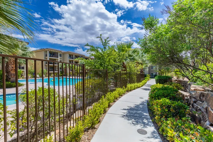 Concrete pathway bordered by lush green landscaping and mature trees