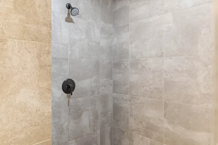 Shower stall featuring large format light gray tile, a coordinating dark bronze shower head, and a dark bronze single-handle control valve