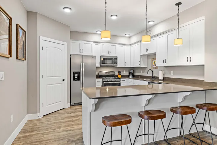 Modern kitchen featuring white shaker cabinetry, stainless steel appliances, a large island with seating, pendant lighting, and wood-finish flooring