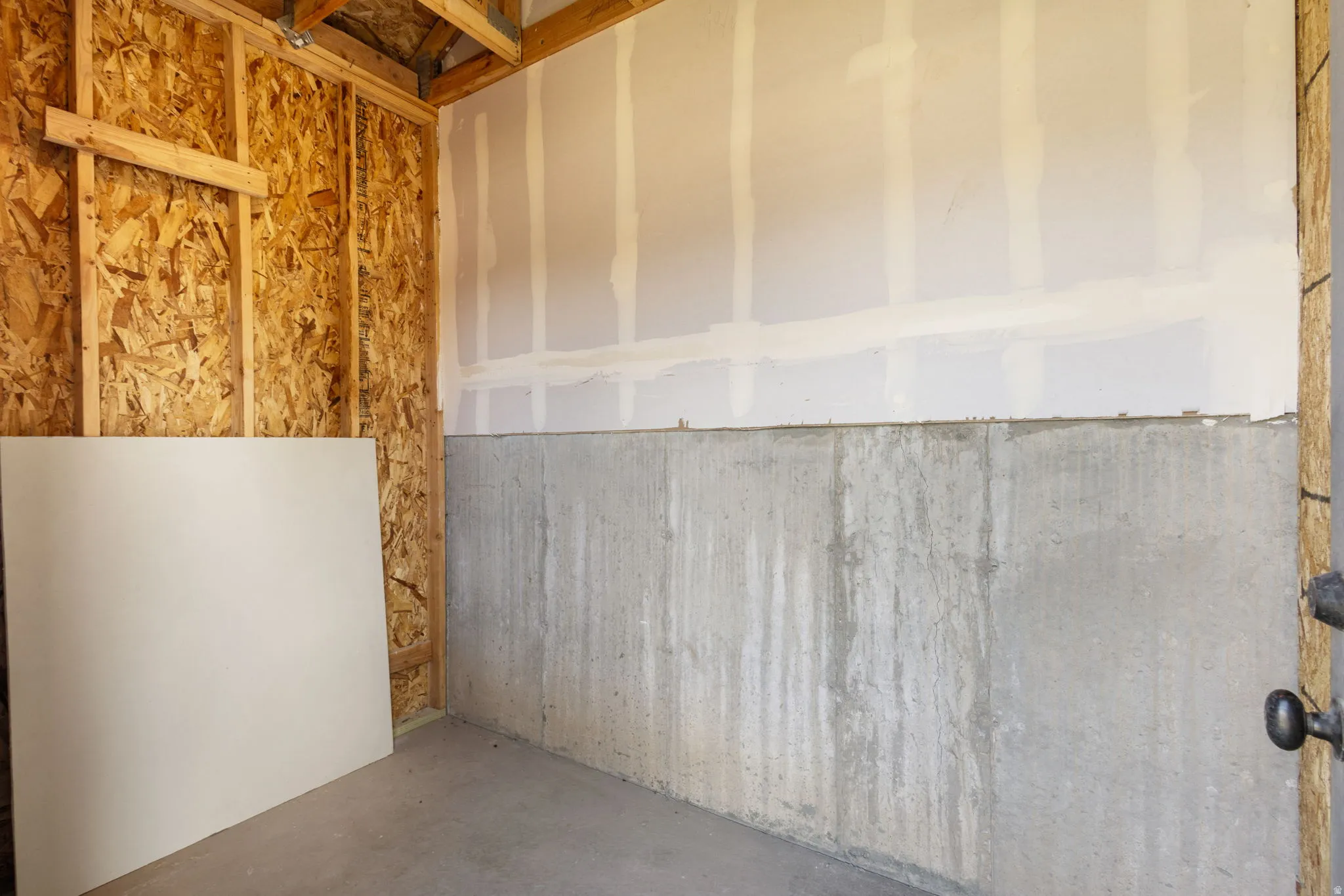 Concrete foundation walls with exposed wood framing and partial drywall installation