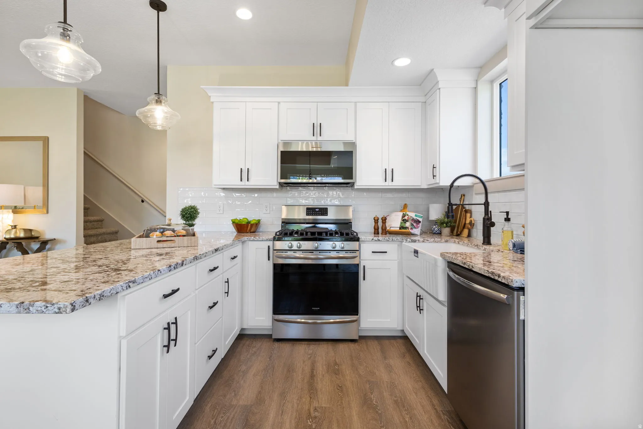 Contemporary kitchen featuring white cabinetry, granite-style countertops, stainless steel appliances, and a farmhouse sink with a matte black faucet