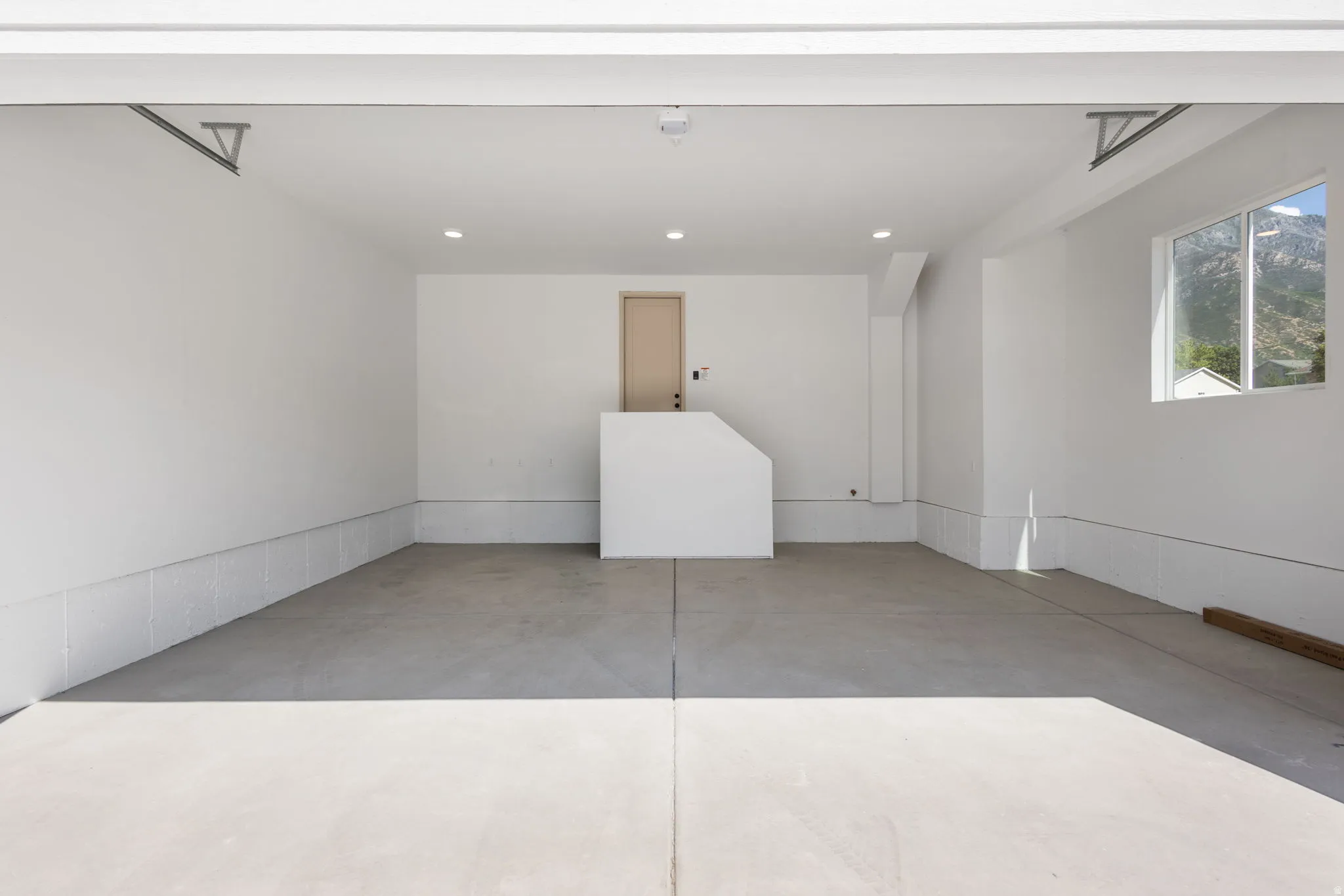 Spacious garage featuring a concrete floor, bright white walls, recessed ceiling lighting, a rear entry door, and a window providing natural light