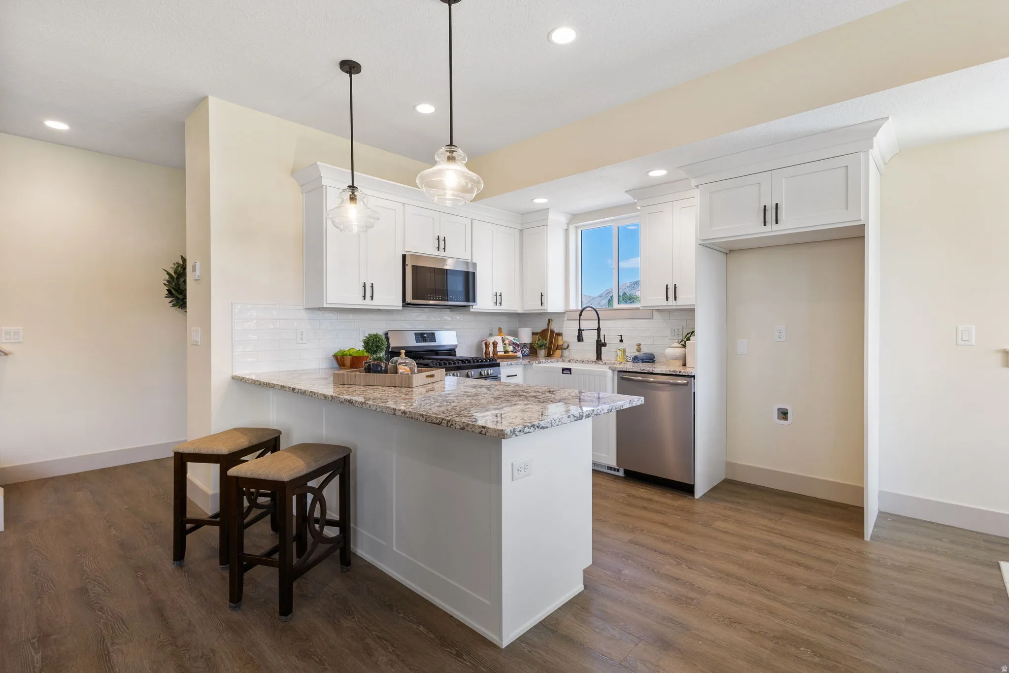 Kitchen featuring white cabinetry, stone countertops, stainless steel appliances, a white subway tile backsplash, and wood-finish flooring