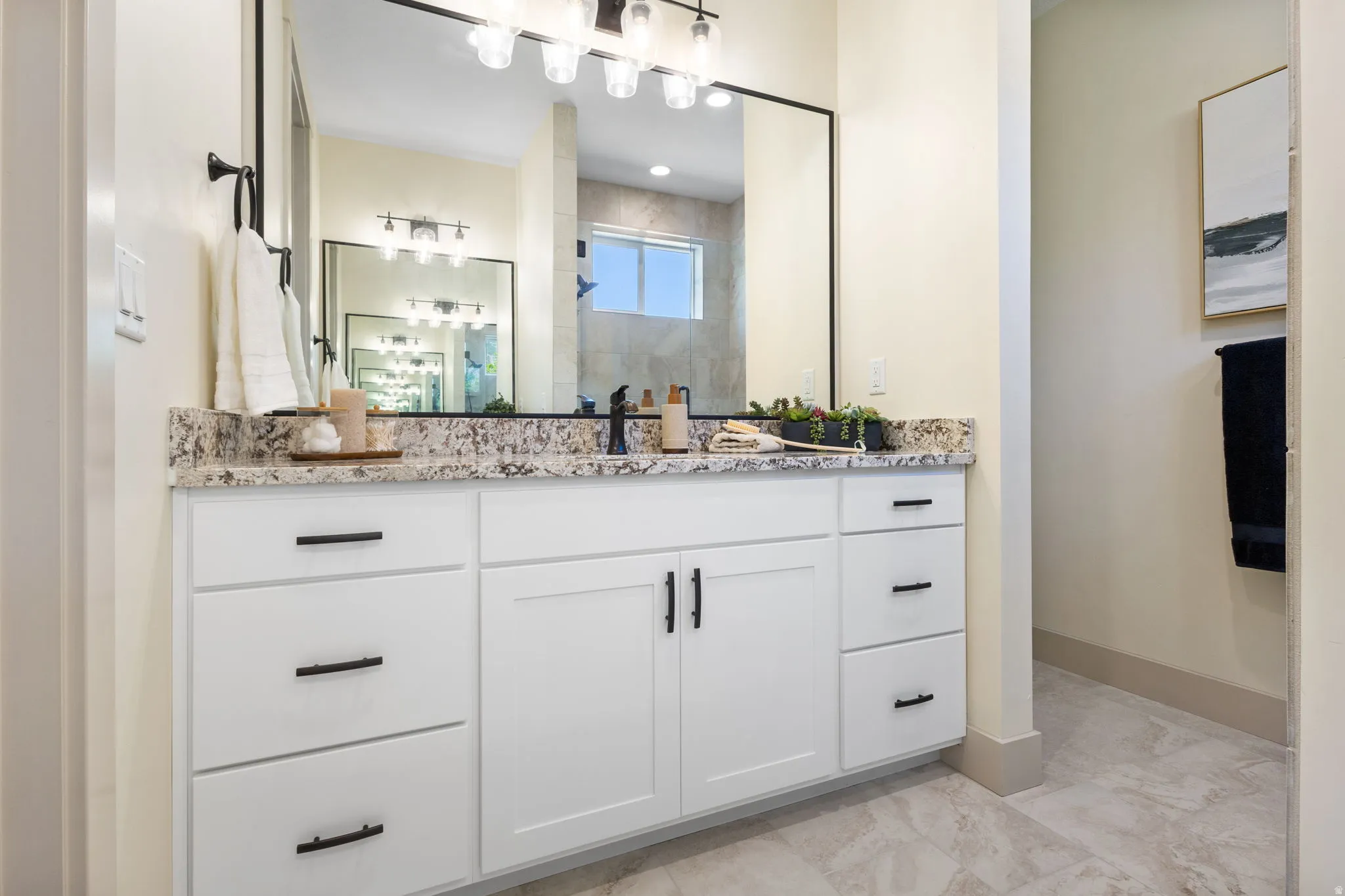 Expansive vanity featuring white cabinetry with matte black hardware, a speckled stone countertop, and a large rectangular mirror