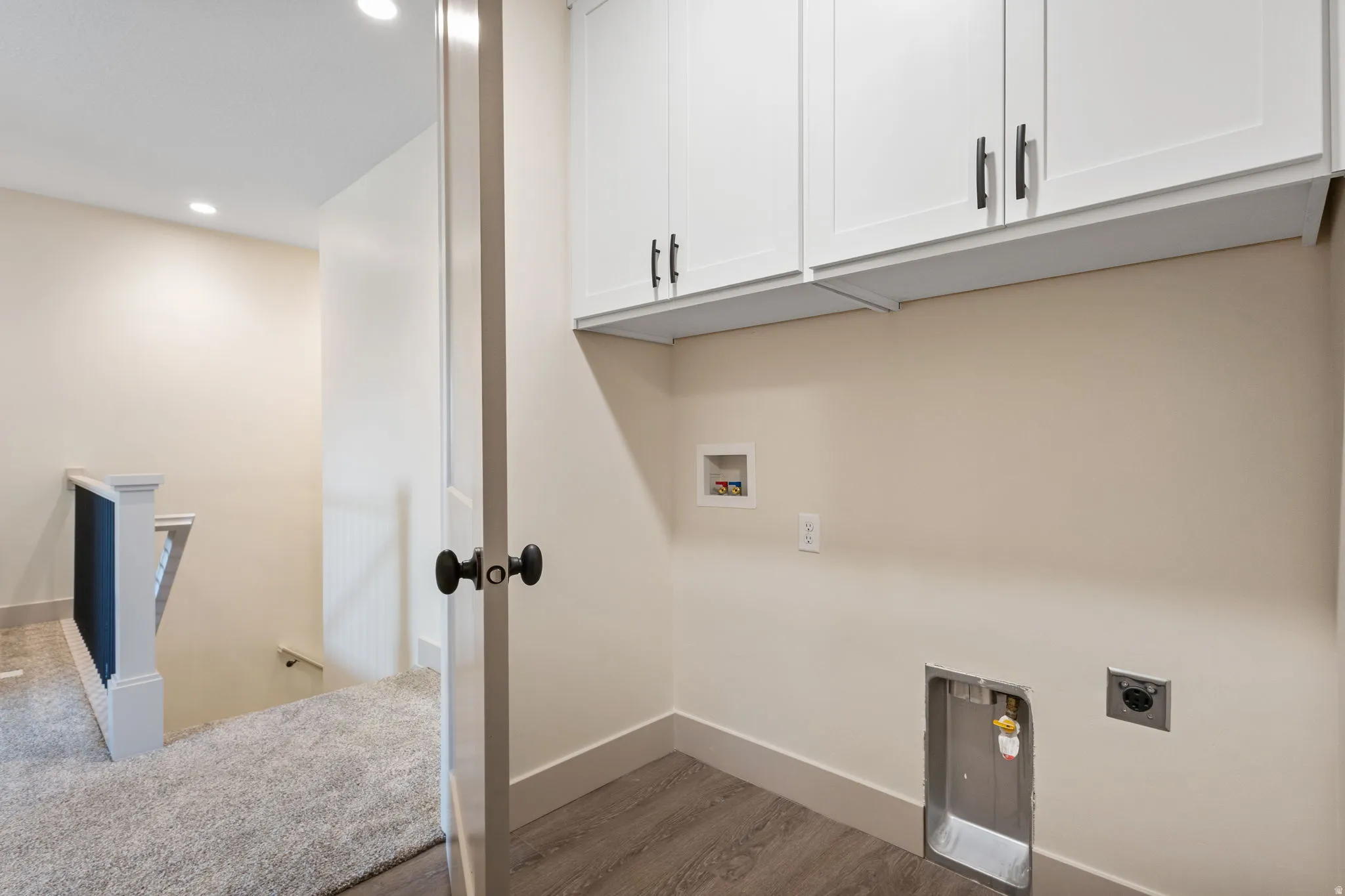 Utility area featuring white shaker-style cabinetry with matte black hardware, wood-finish flooring, and recessed ceiling lighting