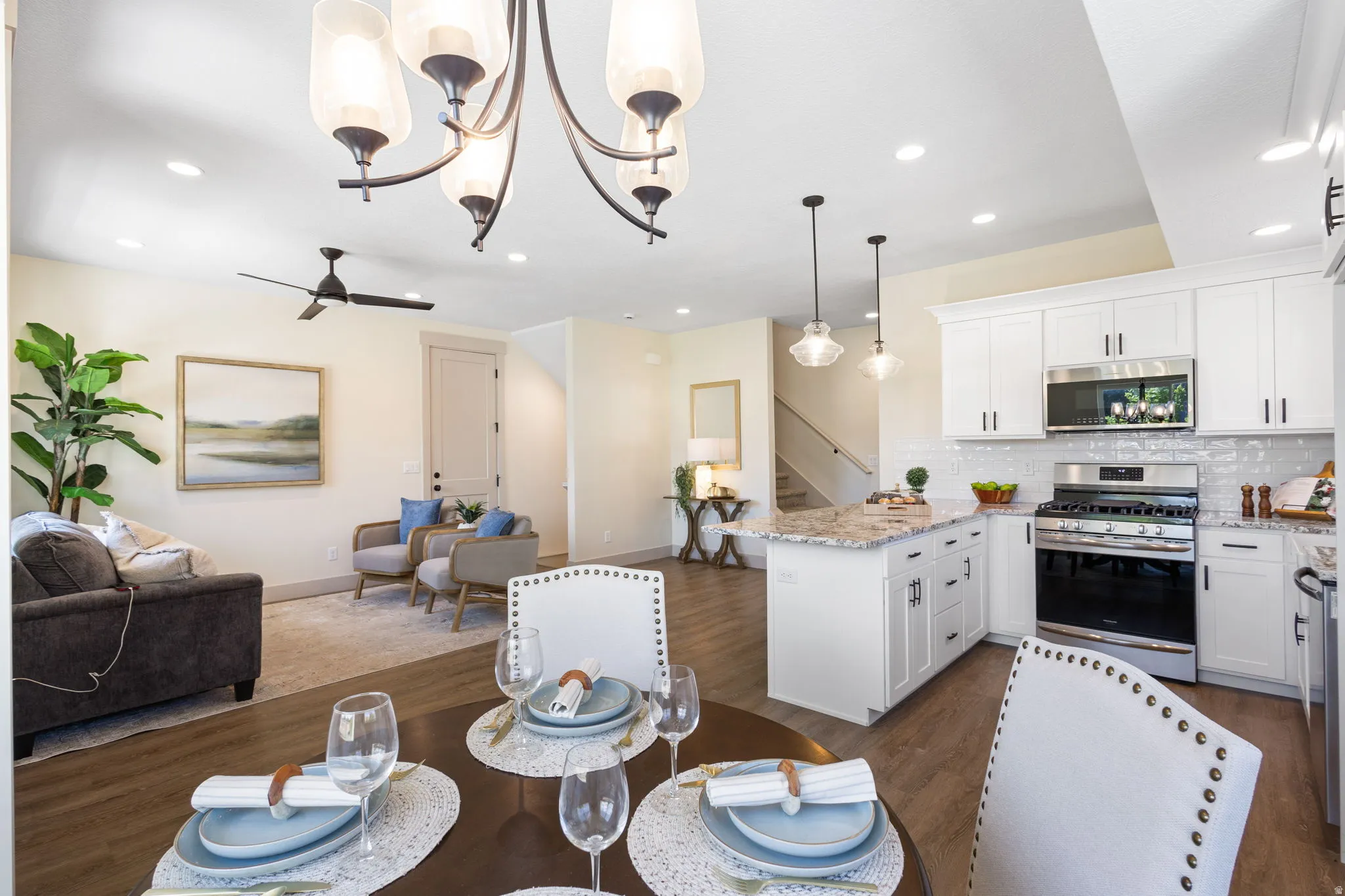 Open-concept living space featuring wood-finish flooring, white shaker cabinetry, stainless steel appliances, and a kitchen island with a stone countertop