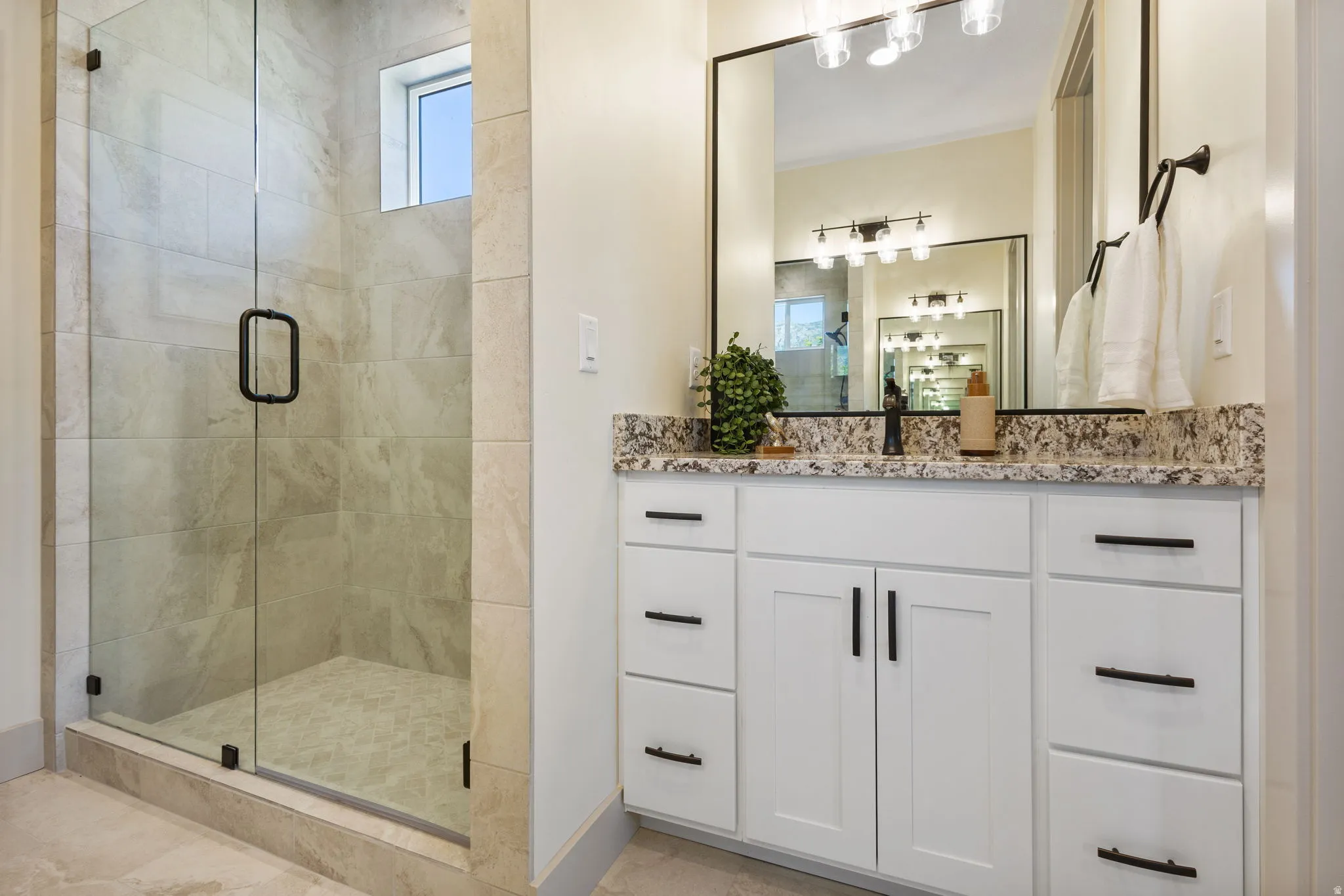 Spacious bathroom featuring a frameless glass shower enclosure, large format tile walls, and a window