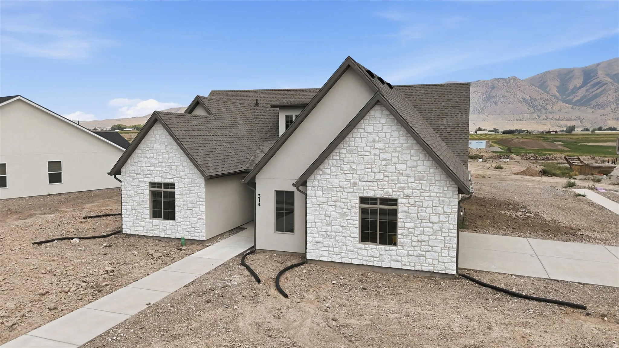 Contemporary home featuring a stone and stucco exterior, a gabled roofline, and multiple dark-framed windows