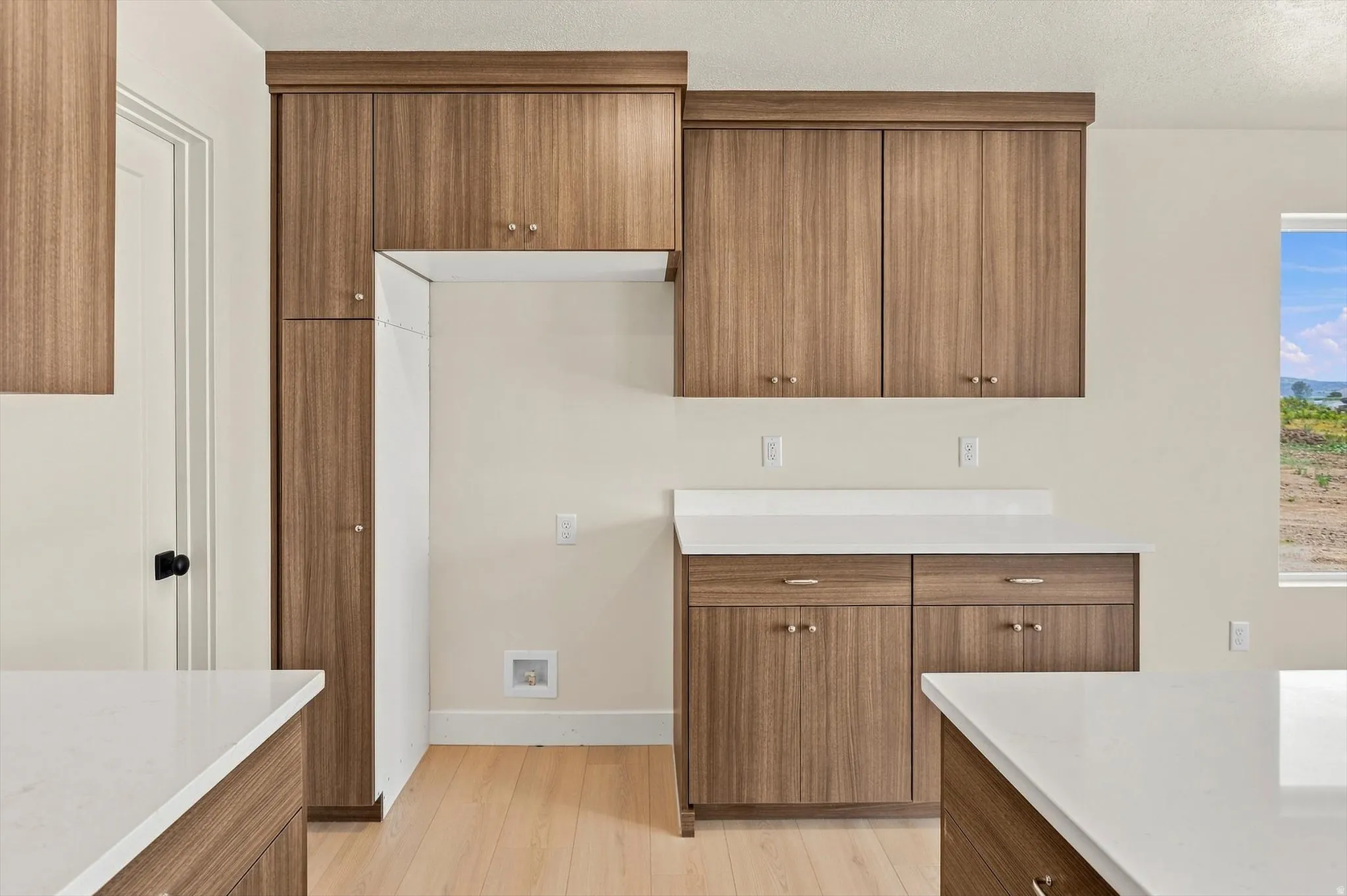Contemporary kitchen featuring wood-grain cabinetry with gold-tone hardware, white countertops, and light wood-finish flooring