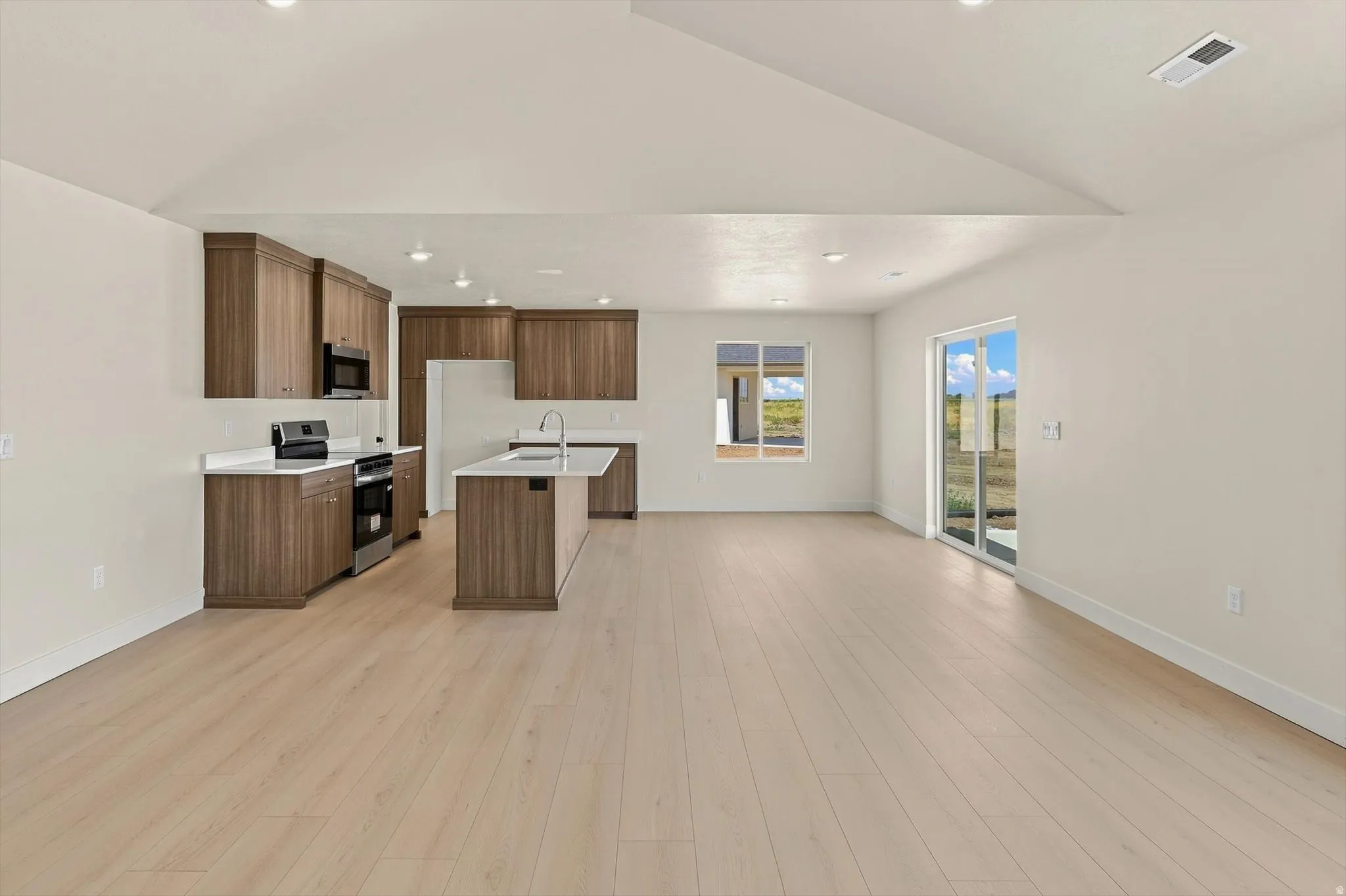 Open-concept kitchen and living area featuring light wood-finish flooring, vaulted ceilings, and recessed lighting