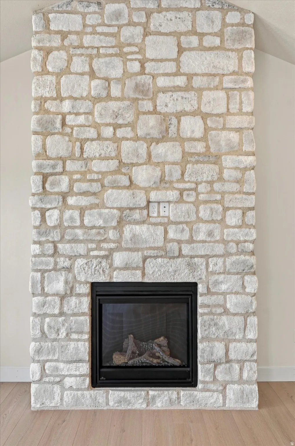 Stone-clad fireplace with an integrated black firebox and gas logs, complemented by light wood-finish flooring