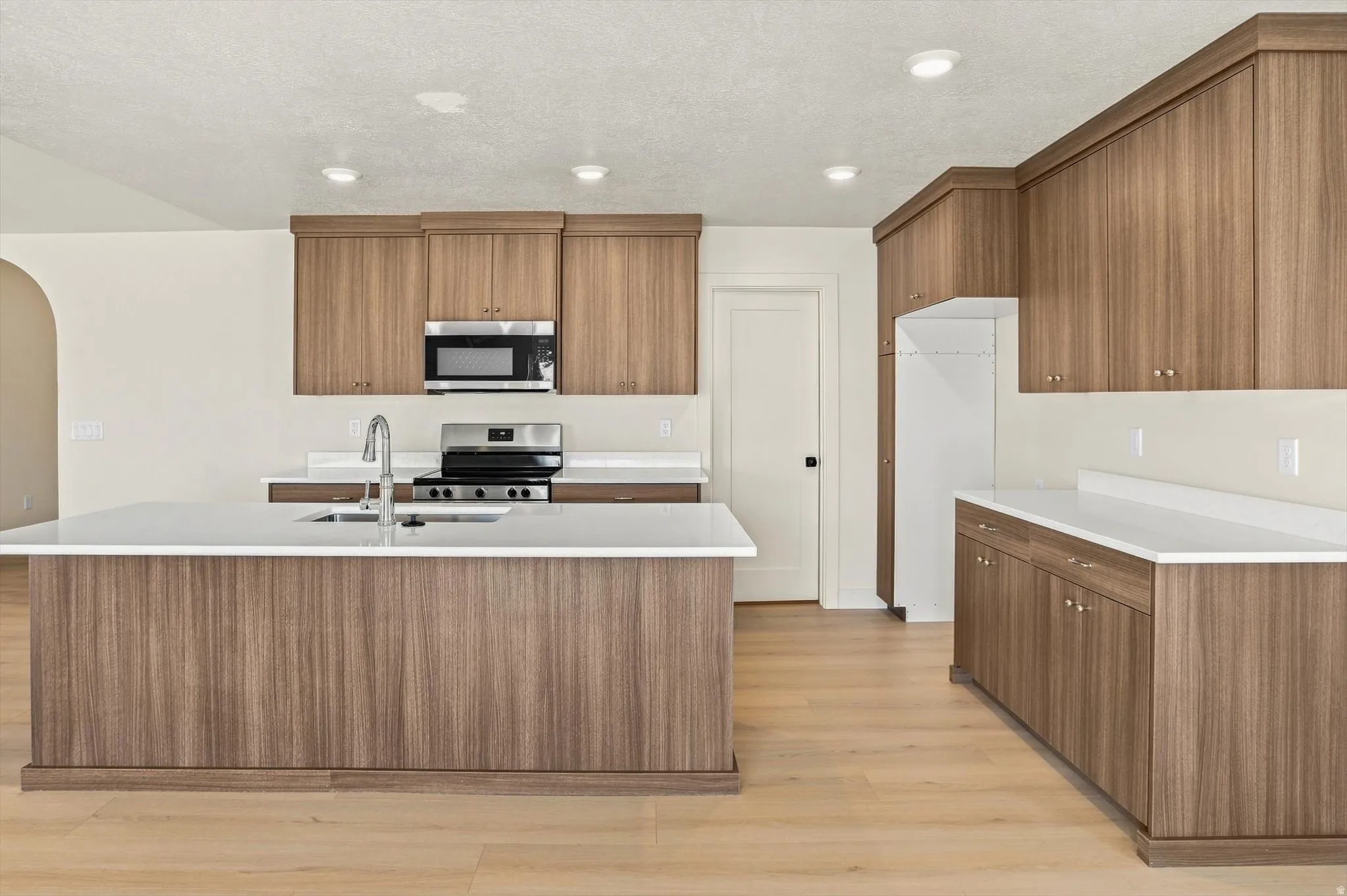 Modern kitchen featuring a central island with an undermount sink, light wood-finish flooring, recessed lighting, white countertops, and stainless steel appliances