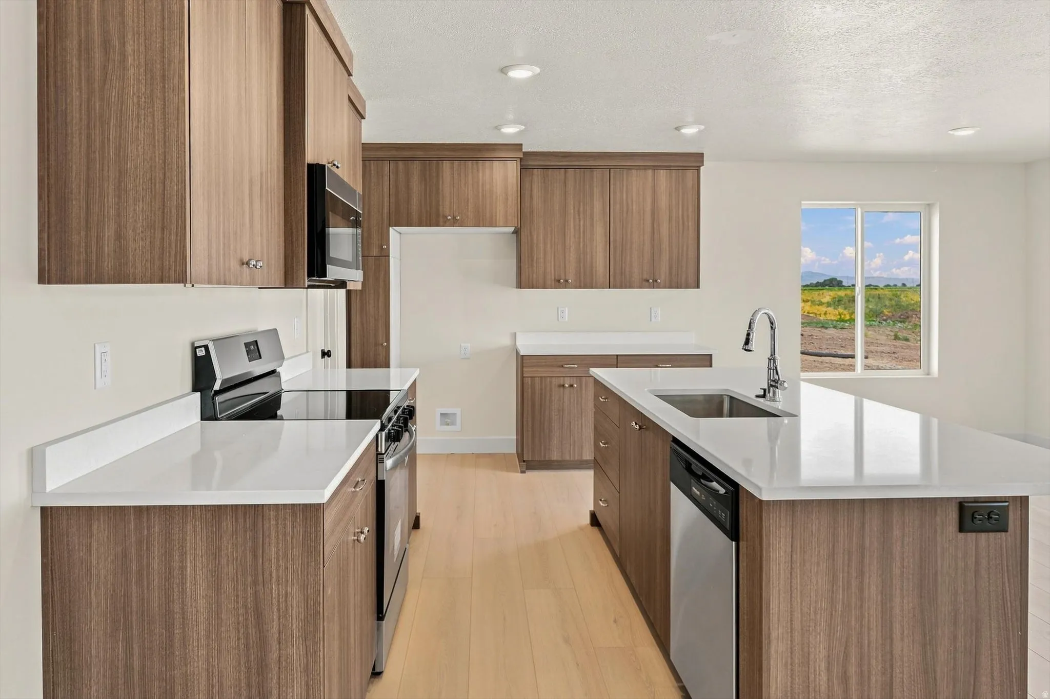 Modern kitchen featuring wood-finish cabinetry, light-toned wood-finish flooring, white countertops, and stainless steel appliances