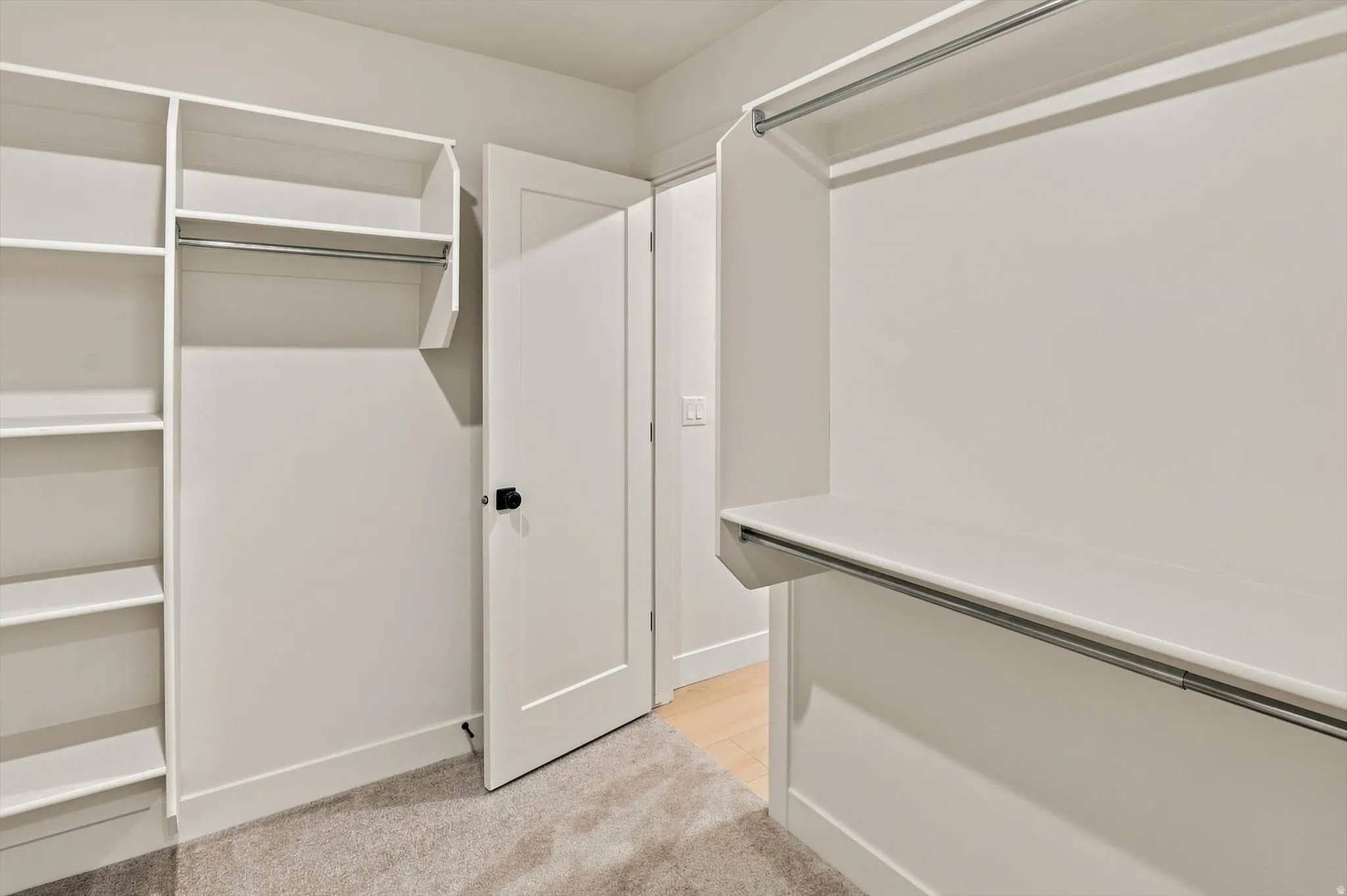 Walk-in closet featuring white built-in shelving, multiple hanging rods, and light gray carpeting