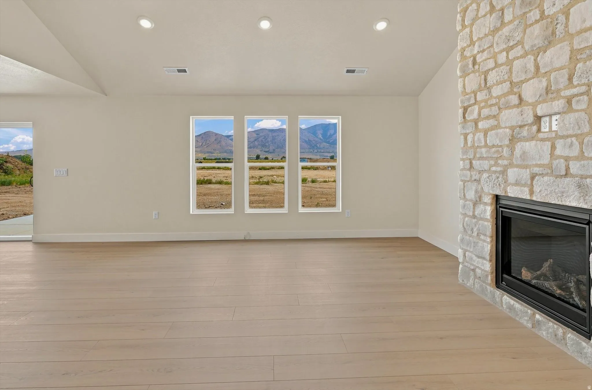 Spacious interior with light wood-finish flooring, a stone-clad fireplace with a black insert, and recessed ceiling lighting