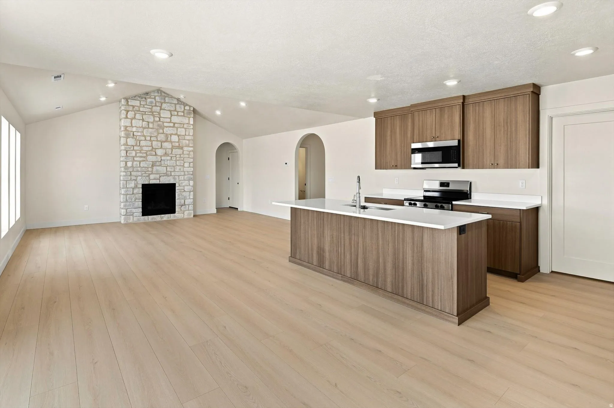 Open-concept living space featuring vaulted ceilings, a stone-clad fireplace, and wood-finish flooring