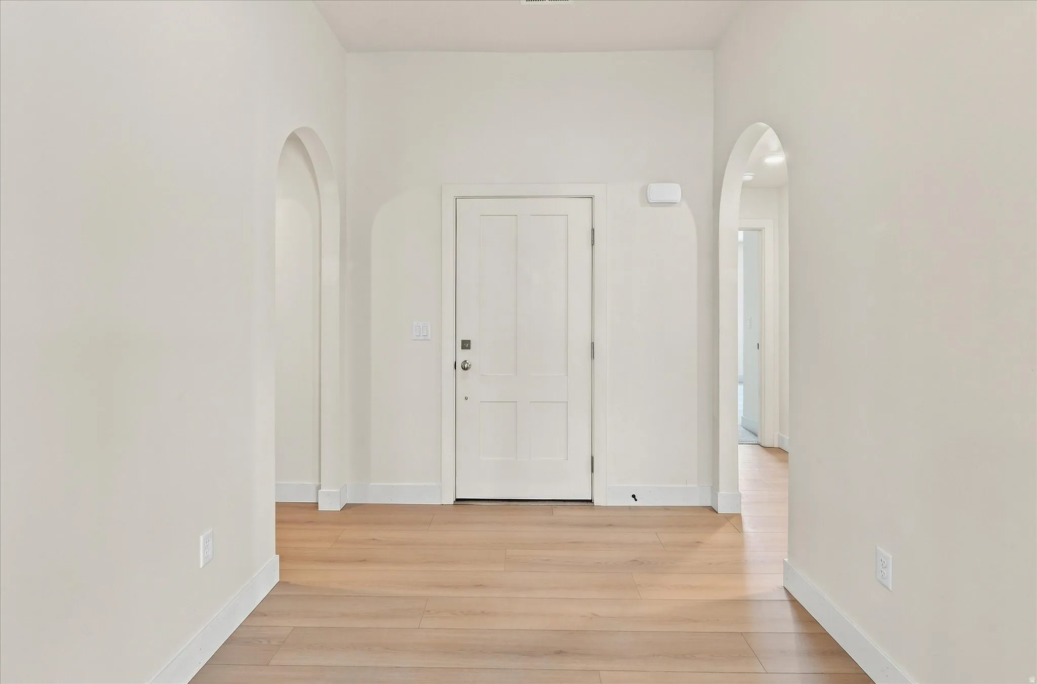 Entryway featuring light wood-finish flooring, white baseboards, and two arched doorways