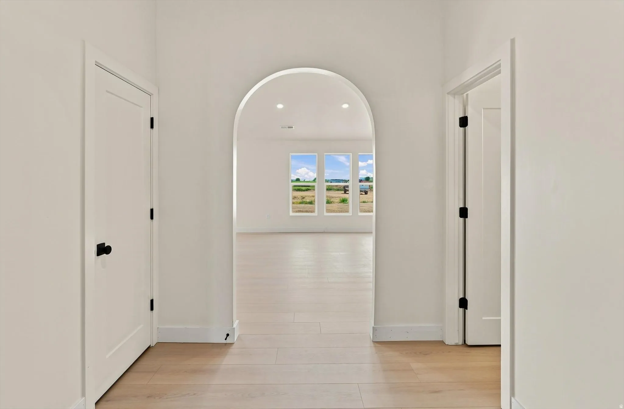 Archway entry to a bright room featuring wood-finish flooring, recessed lighting, and multiple windows