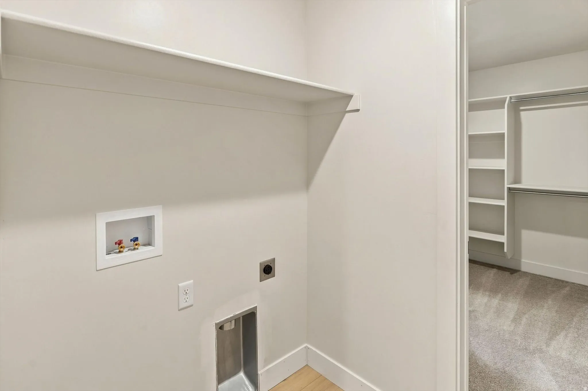 Dedicated laundry area with utility hookups and an integrated shelf, featuring light-colored walls and wood-finish flooring