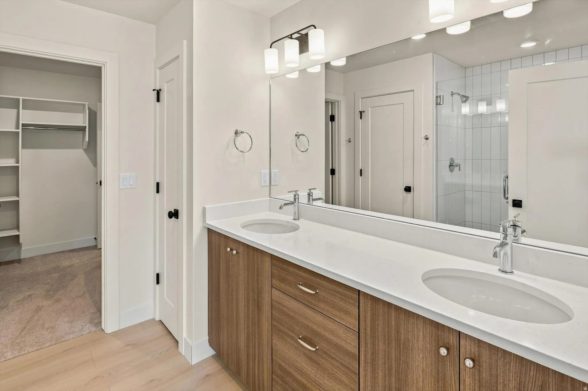 Double vanity with wood-finish cabinetry, white countertops, and chrome fixtures