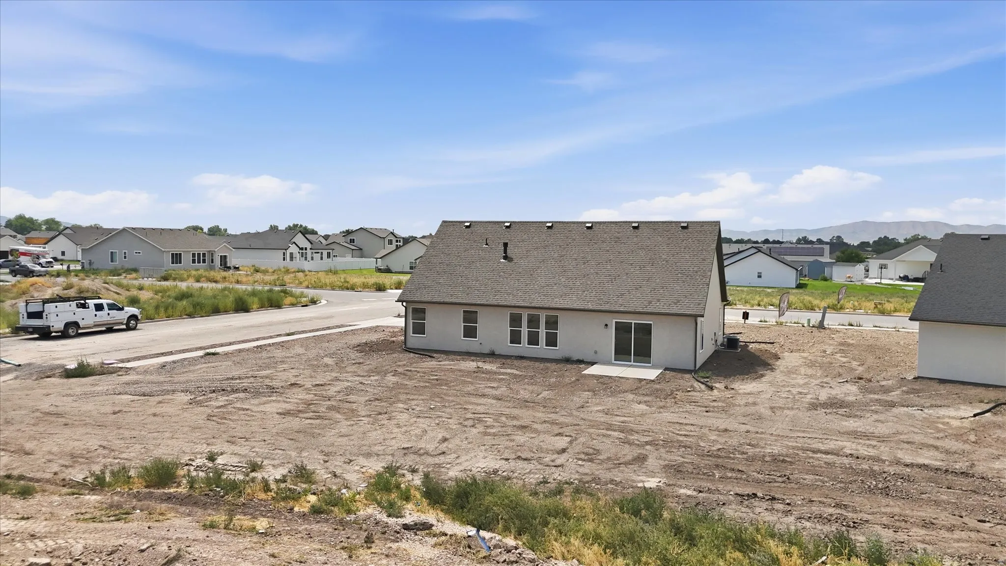 Newly constructed residence featuring a light-colored stucco exterior, a dark shingle roof, and multiple rear windows
