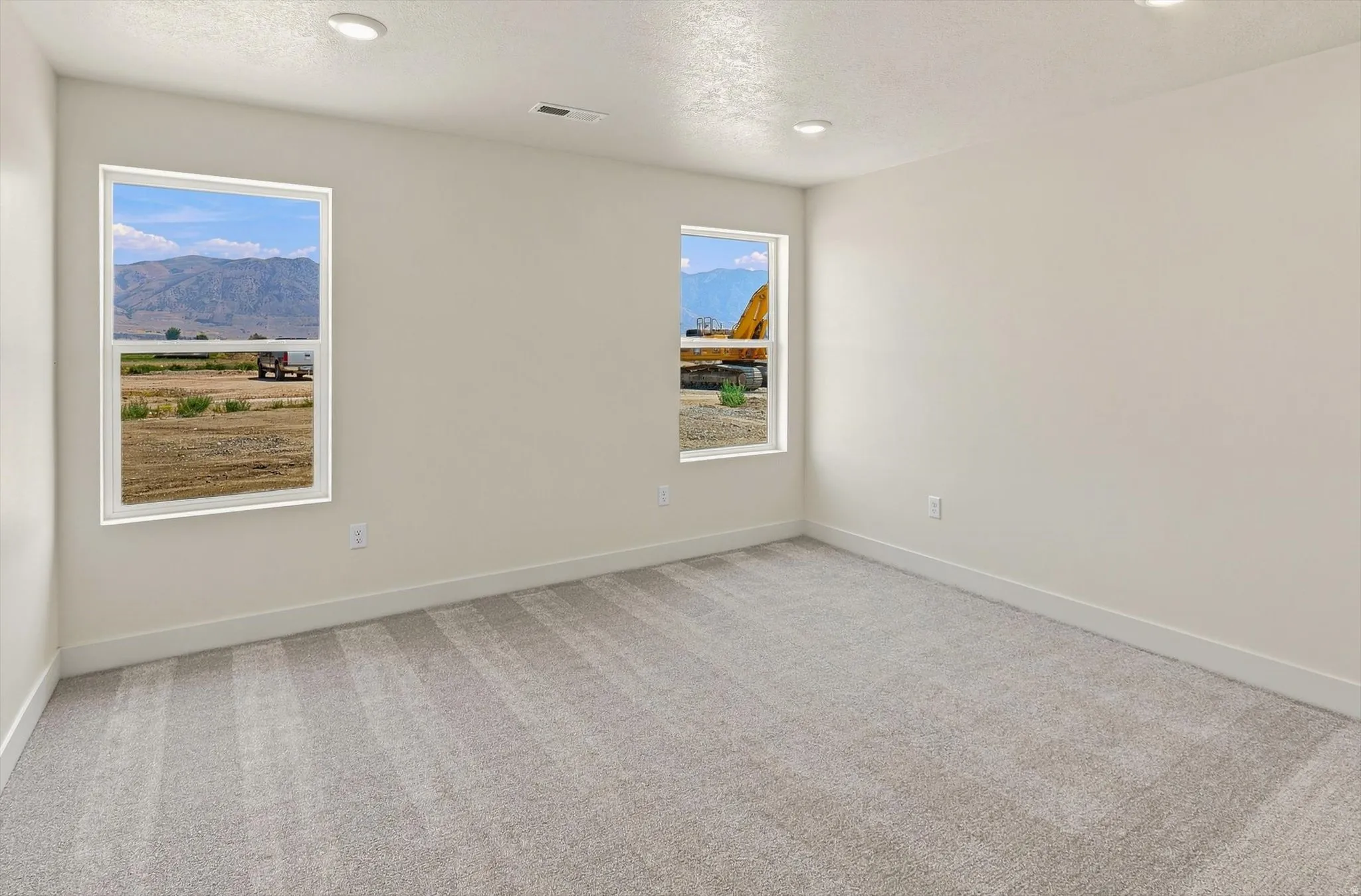 Spacious room with plush gray carpeting, white walls, two large windows, recessed lighting, and mountain scenery visible through the windows