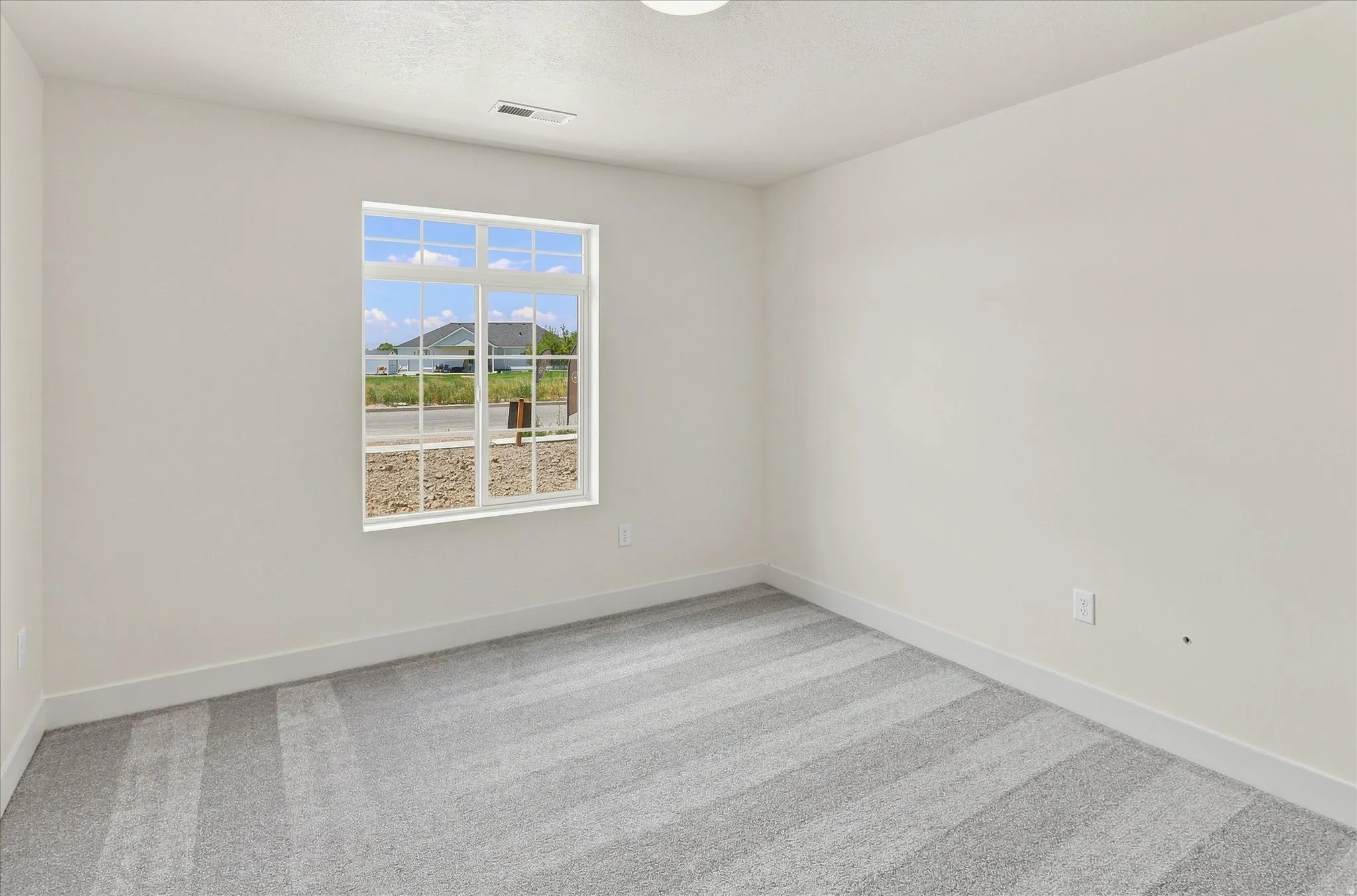 White-painted interior room featuring a multi-pane window with white trim, light-toned walls, gray patterned carpeting, and white baseboards