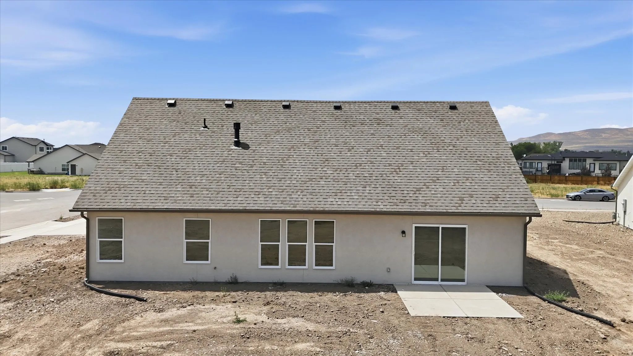 Rear exterior featuring a light-toned stucco facade, multiple windows, a sliding glass door, and a concrete patio