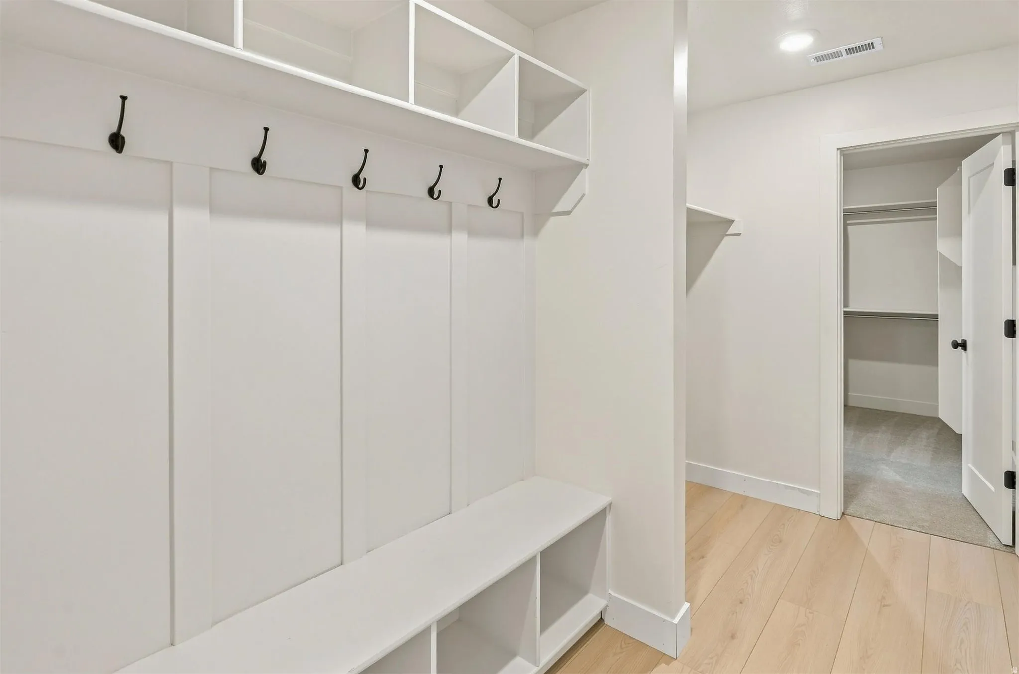 Built-in mudroom bench with cubby storage, upper shelving, and dark-finish coat hooks