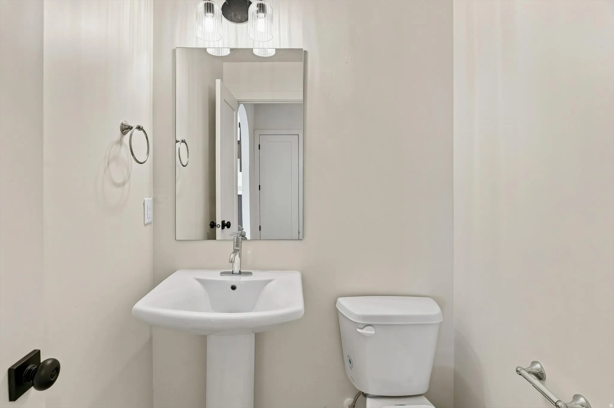 Pedestal sink with chrome faucet, complemented by a rectangular mirror and a two-light vanity fixture