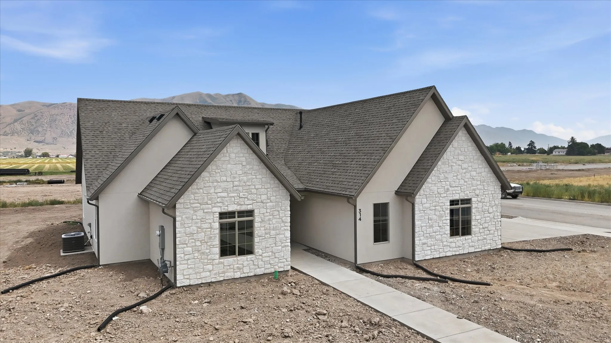 Contemporary exterior featuring light-toned stone accents, stucco siding, a dark shingle roof, and multiple gables