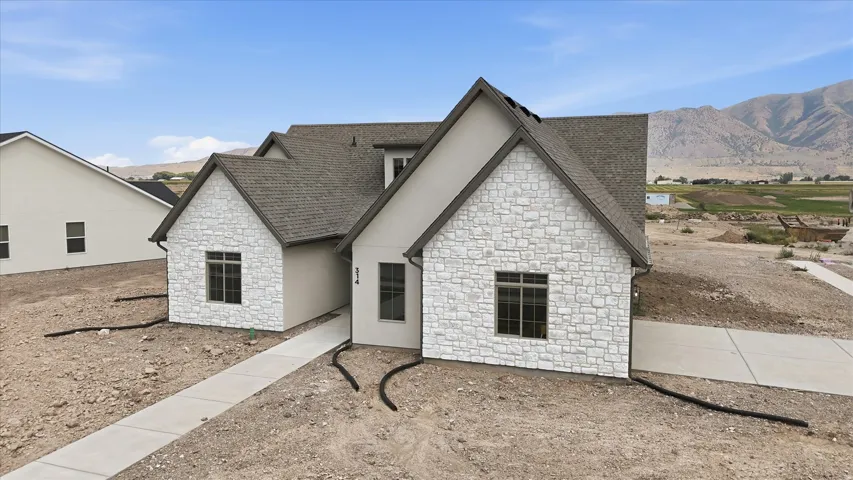 Contemporary home featuring a stone and stucco exterior, a gabled roofline, and multiple dark-framed windows